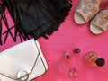 White shoes, white handbag, black leather skirt with fringe on pink background. Perfume, red lipstick, red nail varnish, earrings.