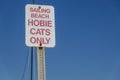 White sign on a metal post that says Sailing Beach Hobie Cats only against a clear cloudless blue sky