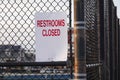 White sign with red lettering that says, Restrooms Closed on a metal chain link fence by a playground Royalty Free Stock Photo