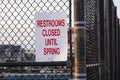 White sign with red lettering that says, Restrooms Closed Until Spring on a metal chain link fence by a playground Royalty Free Stock Photo