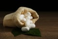 White silk cocoons with sackcloth bag and mulberry leaves on table, closeup