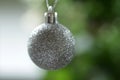 White silver Christmas ball ornament hanging on a blur green tree bokeh light background. Closeup of single Christmas ball Royalty Free Stock Photo