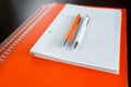 White sketchbook and orange notebooks lying on a dark brown wooden table with an orange and white pens Royalty Free Stock Photo