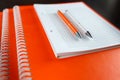 White sketchbook and orange notebooks lying on a dark brown wooden table with an orange and white pens Royalty Free Stock Photo