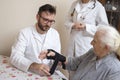 White-skinned nurse uses a stabilizer on the wrist of an old woman under the supervision of a doctor.