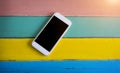 White Smart phone with blank screen lying on colourful wooden ta Royalty Free Stock Photo