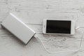 White smart phone charging from silver power bank charger on wooden background. Productive portable charging device for travel Royalty Free Stock Photo