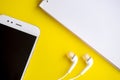 White smart phone and headphones with notepad and pencils on the yellow background.