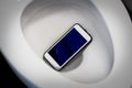 A white smartphone dropped into a toilet bowl. Royalty Free Stock Photo