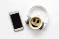 White smartphone with blank mock up screen, headphones, cup of coffee with smile face on white background. Top view. Copy space Royalty Free Stock Photo
