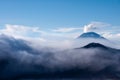 White smoke coming out of volcanoes surrounded by white clouds of mist and a clear blue sky.