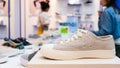 White sneakers on the display table in the fashion shoes store, close-up with blurred background of buyer. Costumers in shoes