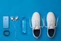 White sneakers, headphones, smart bracelet and water bottle on blue background. Sports style. Flat lay.