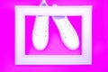 White sneakers and wooden frame on neon pink background. Royalty Free Stock Photo