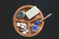 White soap, seshels, bottle, lavender salts and wooden spoon on the wooden round form. Black background