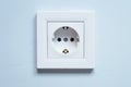 White socket with grounding contacts on a blue wall background. Electricity consumption concept