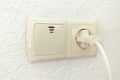 White socket with plug and light switch on an empty wall with space for text Royalty Free Stock Photo
