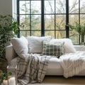 White sofa with plaid and cushions on knitted rug against of grid window between green houseplants. Scandinavian, hygge design Royalty Free Stock Photo