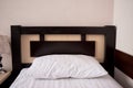 White soft pillow on single bed with brown wooden headboard in hotel bedroom interior, copy space. Classic lamp on bedside table