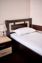 White soft pillow on single bed with brown wooden headboard in hotel bedroom interior, copy space. Classic lamp on bedside table.