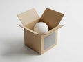 A white sphere nestled inside an open top brown cardboard box on a light-colored surface Royalty Free Stock Photo