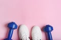 White sport sneakers shoes and blue dumbbells on the pink background. Royalty Free Stock Photo