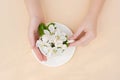 White spring apple trees blooming flowers in a coffee cup in female elegant hands on a beige background. Spring summer concept.