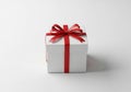 A white square gift box sits on a plain surface. It is adorned with a red ribbon that wraps around Royalty Free Stock Photo