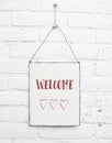 White square metal plate on white brick background - with text welcome and three cute red hearts