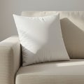 A white, square pillow rests on a beige fabric sofa. The sofa has a textured surface, w Royalty Free Stock Photo