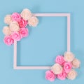 White square shaped picture frame surrounded by pink and white foam rose flower blossoms on blue background