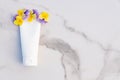 White squeeze bottle cosmetic cream tube and pansy flowers on marble background with copy space. Top view. Unbranded lotion,