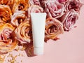 White squeeze bottle cosmetic tube and beautiful large golden pink roses on pastel pink background. Luxury mockup cosmetic