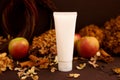 White squeeze cosmetic tube, autumn leaves, cinnamon, apples and dry hydrangea flowers on dark brown background, top view. White