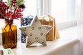 White star with light bulbs on the windowsill against the background of gifts and with a brown vase and red flowers on a twig