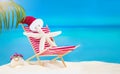 White starfish with Santa\' hat on striped red sun lounger with puffer fish on sandy beach with palm tree behind sea Royalty Free Stock Photo