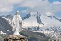 White statue of Virgin Mary, Mother of God, placed on top of the mountain. In the background there are snowy peaks. Royalty Free Stock Photo