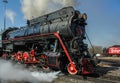 Black iron old train with red details are departing from the station. Steam comes under the wheels. Royalty Free Stock Photo