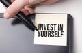 white sticker on the monitor in the office with text Invest in Yourself and hand with marker