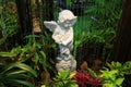 White Stone Angel Sculpture in the Garden Fountain Among Many Green and Red Plants Royalty Free Stock Photo