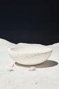 White stone bowl sits on white sand surface. Dark background suggests outer space with small rocks nearby casting shadows. Royalty Free Stock Photo