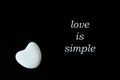 White stone heart on black background with the words `love is simple`.