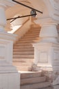 A white stone marble bright classic staircase are leading up with a curve and pillars with an ornament. Sunrays are passing