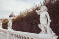 White stone statues of boys in the park. The nearest of them with a horn, a gun and a hunting dog. On the background is a dome of