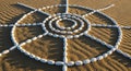 White stones are arranged in a circular geometric pattern on rippled sand, creating a sun-like Royalty Free Stock Photo