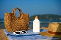 Woven bag, sunscreen bottle, straw, on blue towel beside sea. White sunglasses on sand embody summer essentials Royalty Free Stock Photo