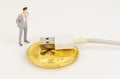 On a white surface are a bitcoin cord with USB and a miniature human figure. Royalty Free Stock Photo