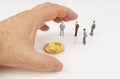 On a white surface, bitcoin, miniature figures of people and a human hand that reaches for bitcoin.