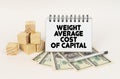 On a white surface, cubes, dollars, a pen and a notepad with the inscription - WEIGHT AVERAGE COST OF CAPITAL