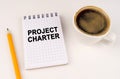 On a white surface, a cup of coffee, a pencil and a notepad with the inscription - PROJECT CHARTER Royalty Free Stock Photo